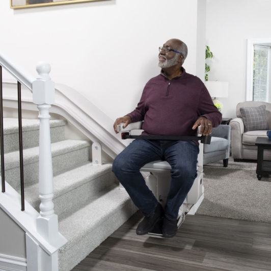 man sitting on stair lift in home and smiling