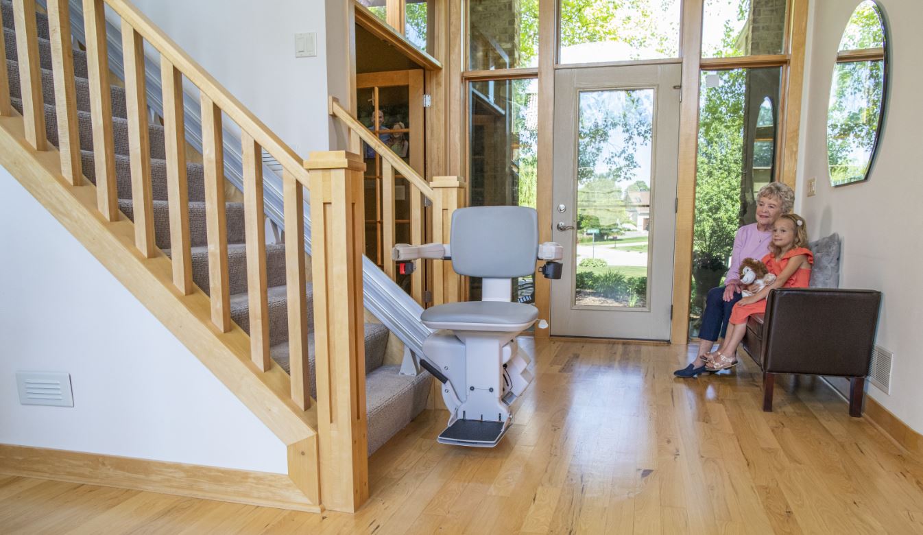 Grandma sitting with grandchild on chair and smiling next to stair lift