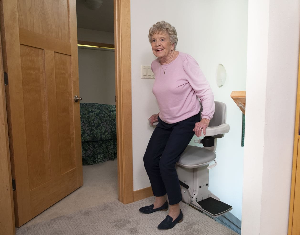 woman safely exits chair of stair lift at top landing of staircase after using power swivel