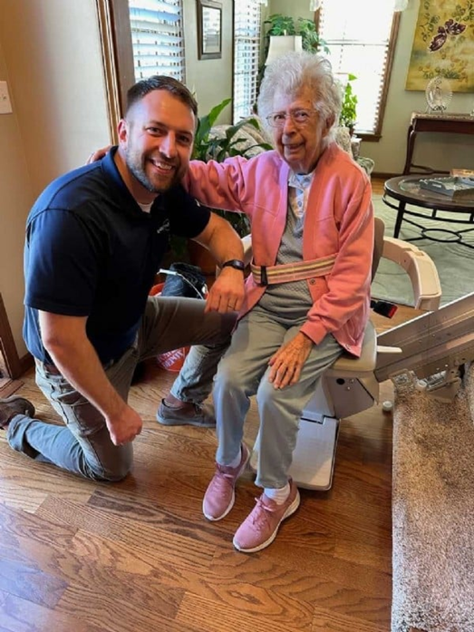 happy woman sits in new stairlift next to Lifeway Mobility technician kneeling beside her