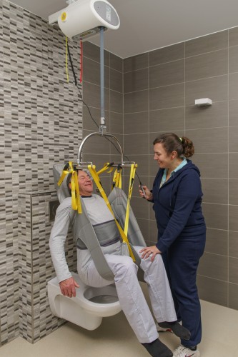 caregiver helping man onto toilet using ceiling mounted lift