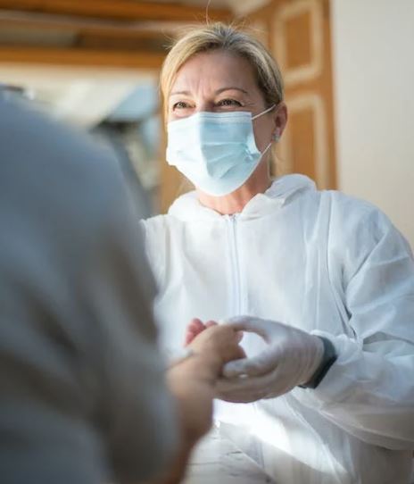 doctor wearing a mask talking and holding hand of cancer patient in their home