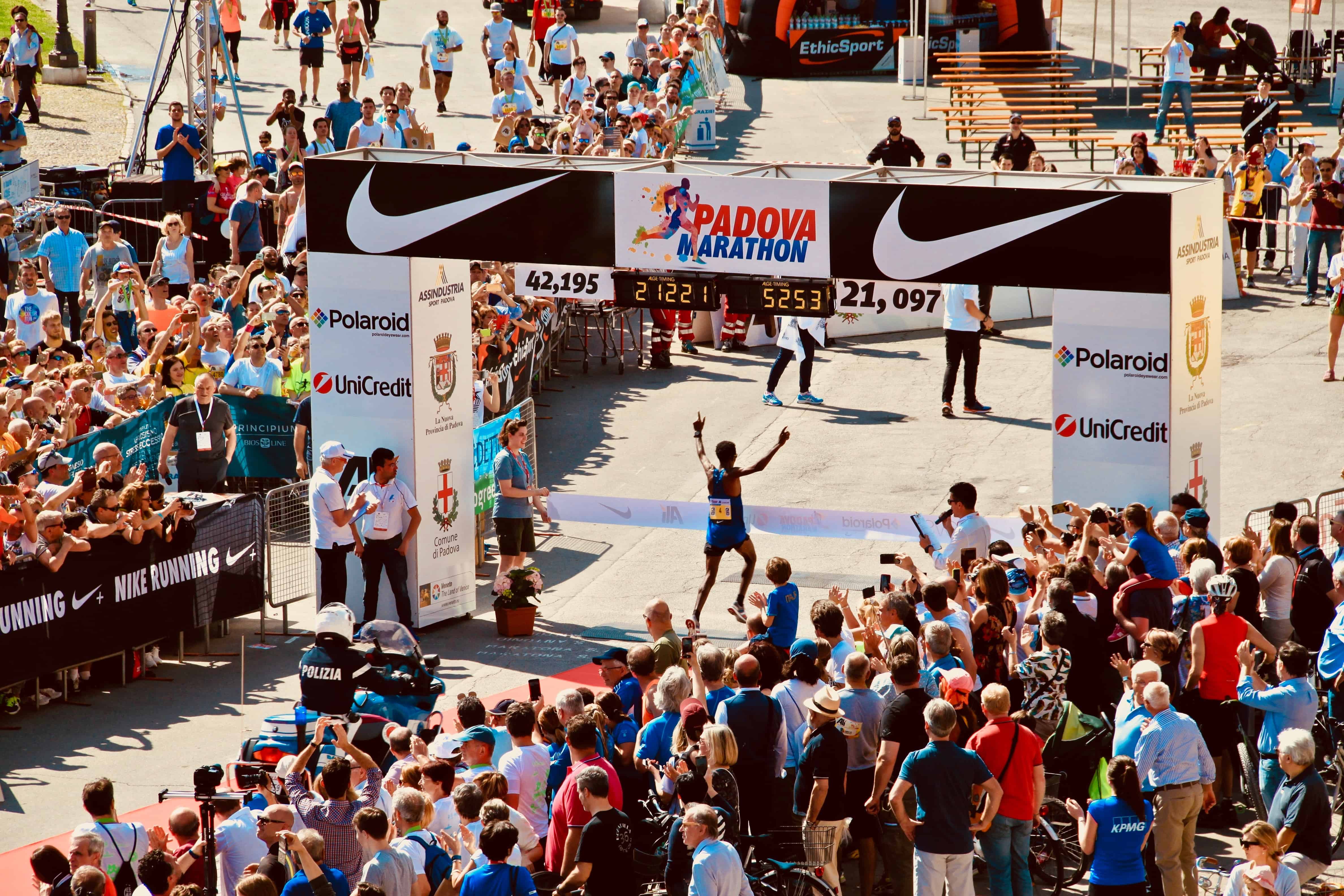 marathon runner puts arms up in celebration as he crosses finish line with fans cheering