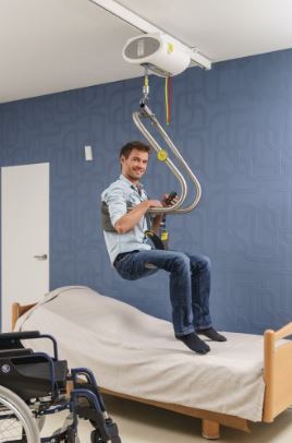 man using fixed ceiling lift to safely transfer from wheelchair to his bad