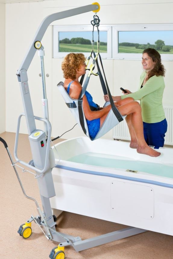 caregiver using mobile patient lift to safely transfer woman into bathtub at home