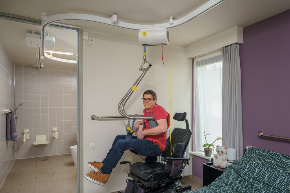 A handicap man is lifted by a SureHands ceiling lift out of his powered wheelchair