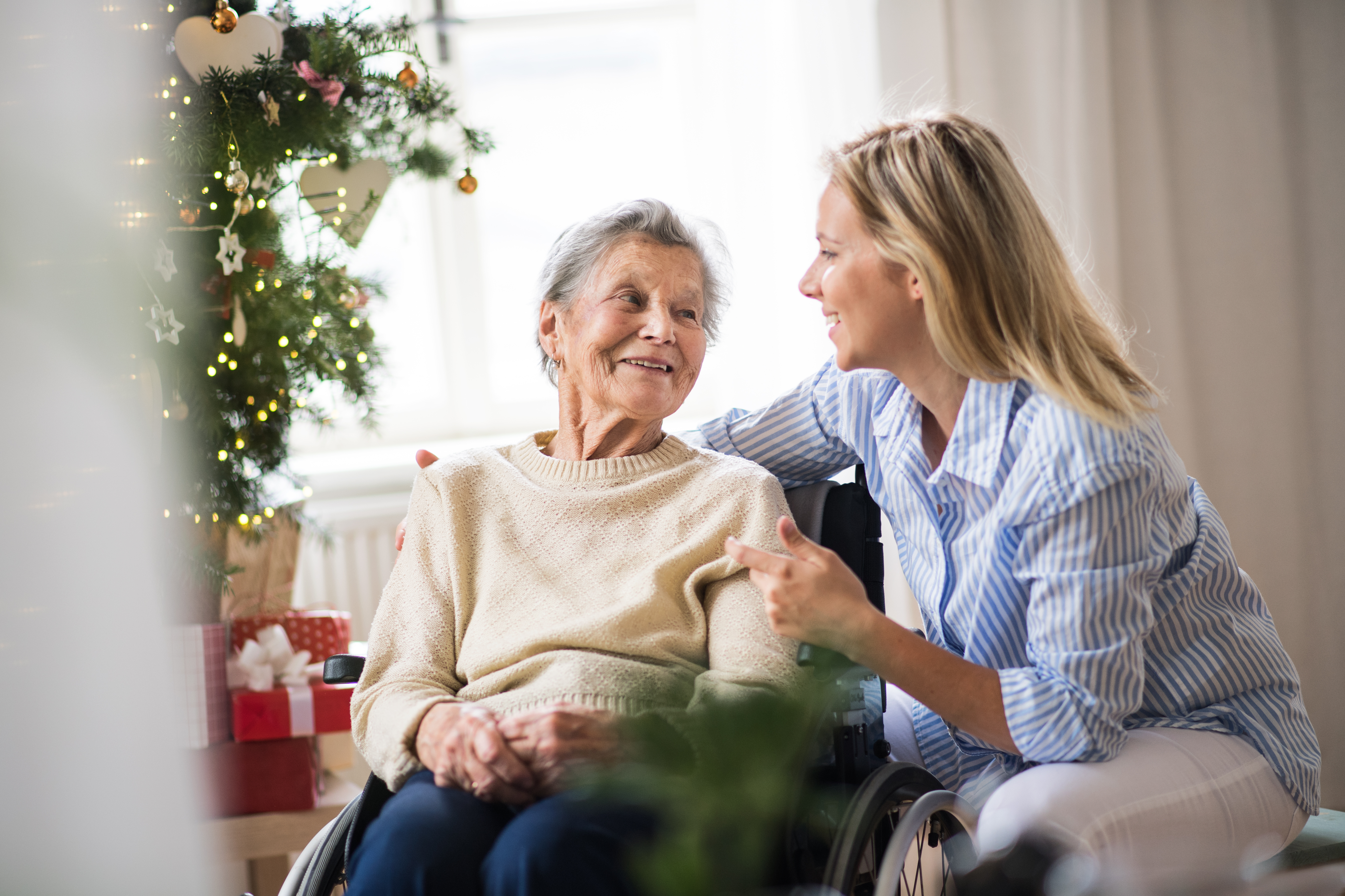 senior woman in wheelchair looking at her adult daughter standing beside her