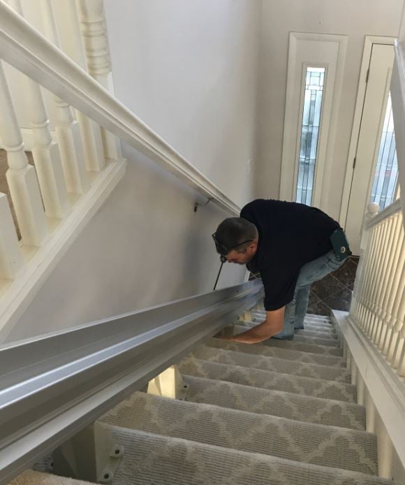 Técnico de movilidad de la vía de elevación instalando el carril de elevación de la escalera en las peldaños de la escalera