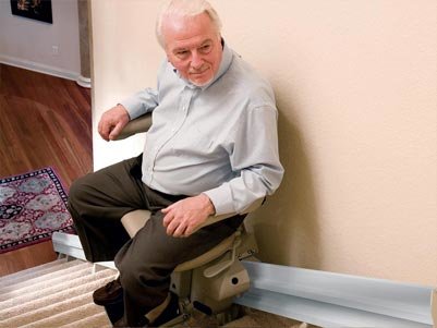 man using rocker switch on armstrest of stair lift to safely reach second level of home