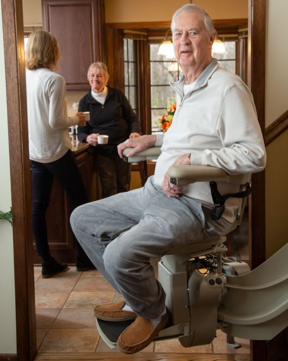 man riding curved stair lift down to kitchen to be with his wife and daughter for a cup of coffee