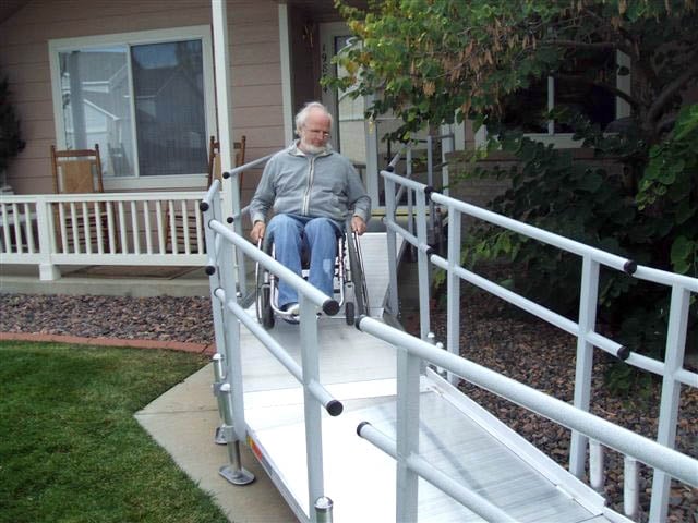 a senior man rides down an aluminum modular wheelchair ramp on his wheelchair at his home 