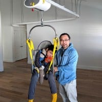 A father stand next to his disabled son that is suspended by a SureHands ceiling lift