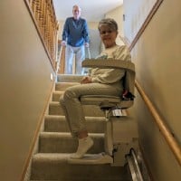 woman smiling and riding new stairlift from Lifeway Mobility while husband waits at top landing