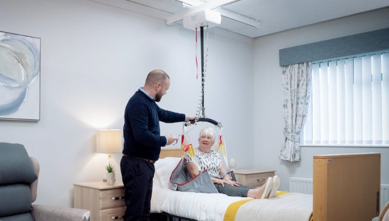 woman sitting in bed waiting to be transferred with a Lifeway Mobility ceiling lift