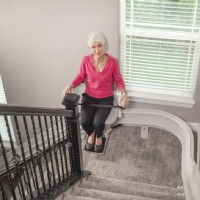 woman riding on new Bruno Elite curved stairlift installed by Lifeway Mobility