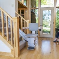 Bruno Elite stairlift at bottom landing lady and grandaughter sitting on bench in background