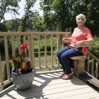woman at top landing of outdoor stairs riding Bruno stairlift