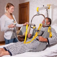 caregiver assists man out of bed using wall lift