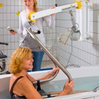 caregiver assists woman into bathroom using wall lift from Lifeway Mobility