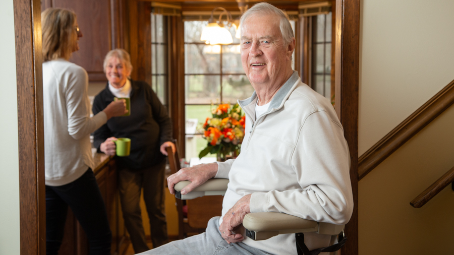 Lifeway Mobility customer riding stairlift while his wife and daughter drink coffee in background