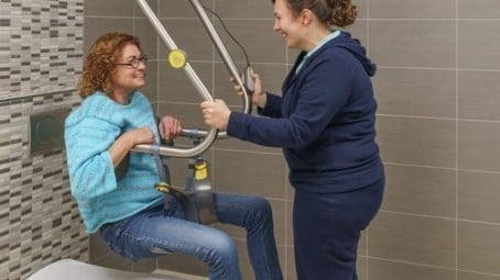 caregiver helps patient safely transfer to toilet using overhead ceiling lift 454 255